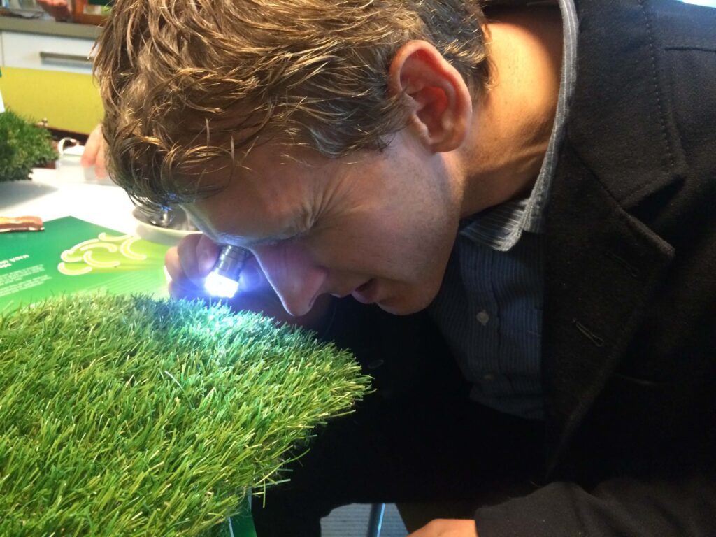Photo of someone looking into a special tool to see the artificial grass fibre present in that artificial grass. 