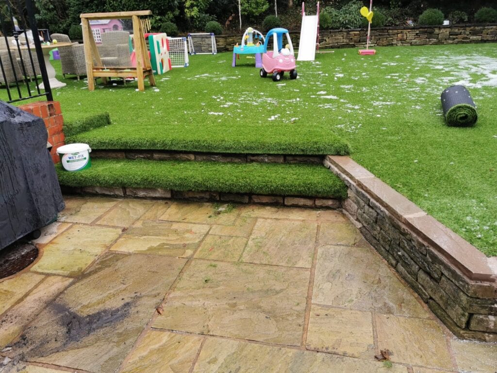 Artificial grass steps, with a dusting of snow in the background on the garden