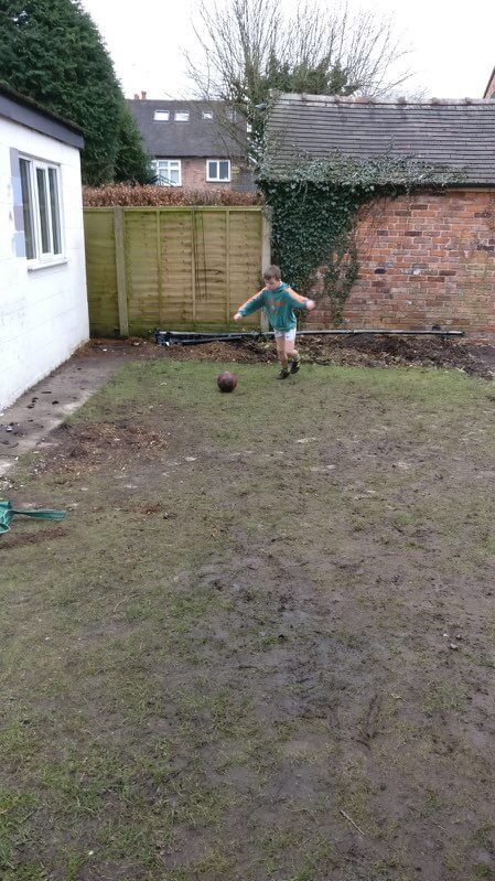 Photo of football crazy kid playing in a mud bath of a garden.